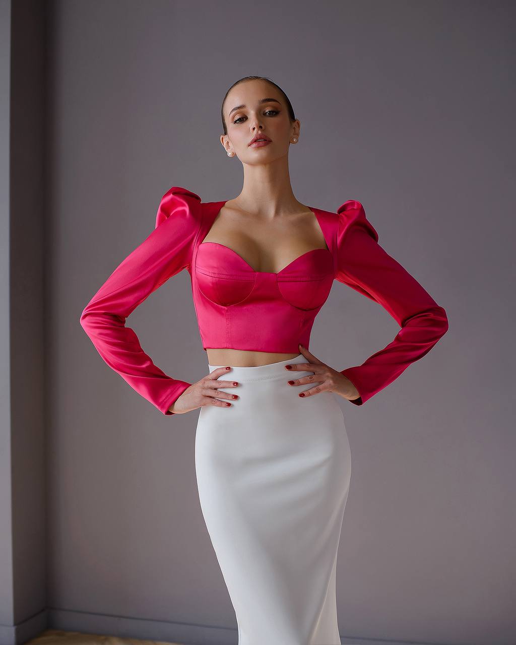 Woman wearing a bright pink top and white skirt against a gray background