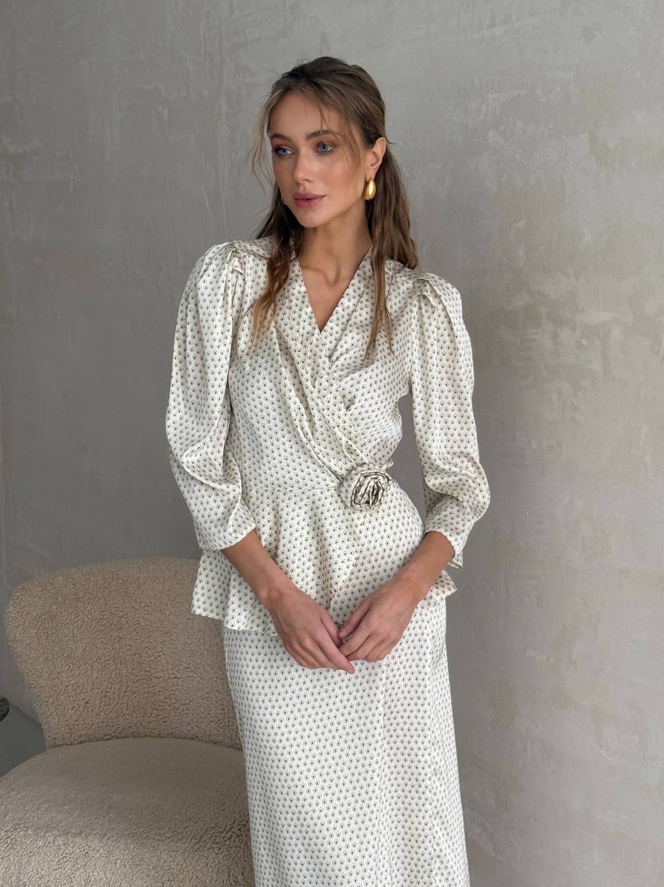 Woman wearing a white polka dot dress against a gray wall.