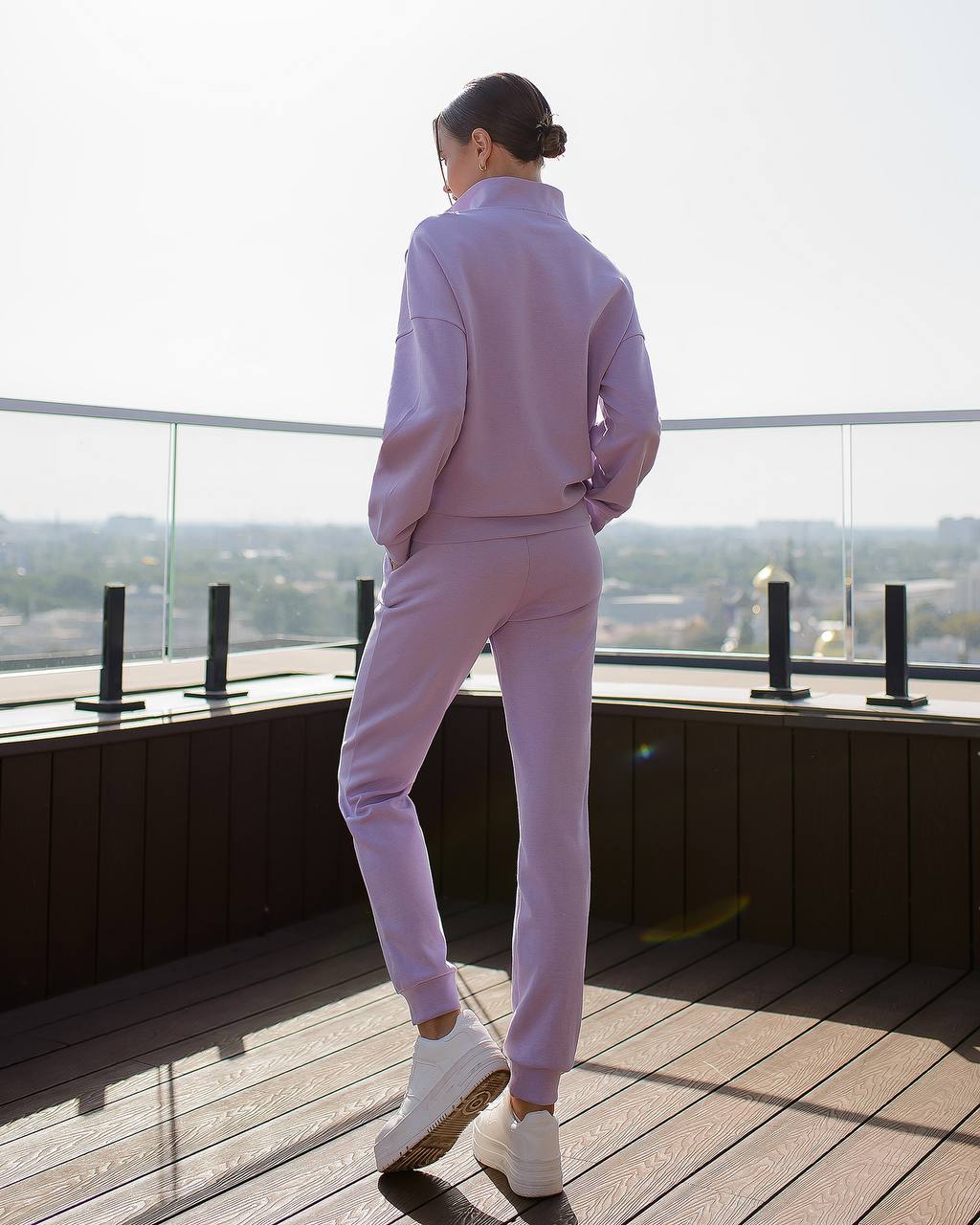 Person wearing a light purple outfit standing on a rooftop with a cityscape view.