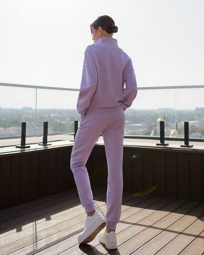 Person wearing a light purple outfit standing on a rooftop with a cityscape view.