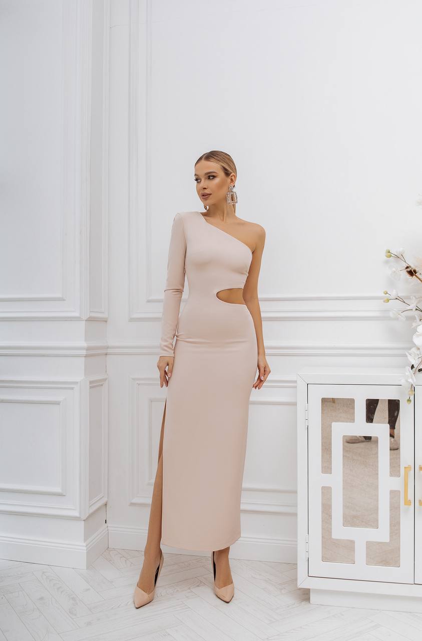 Woman wearing a one-shoulder beige dress in a white room.