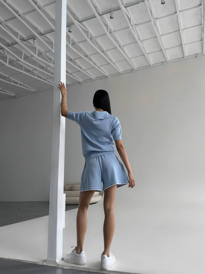 Person wearing a light blue outfit standing in a minimalistic room.