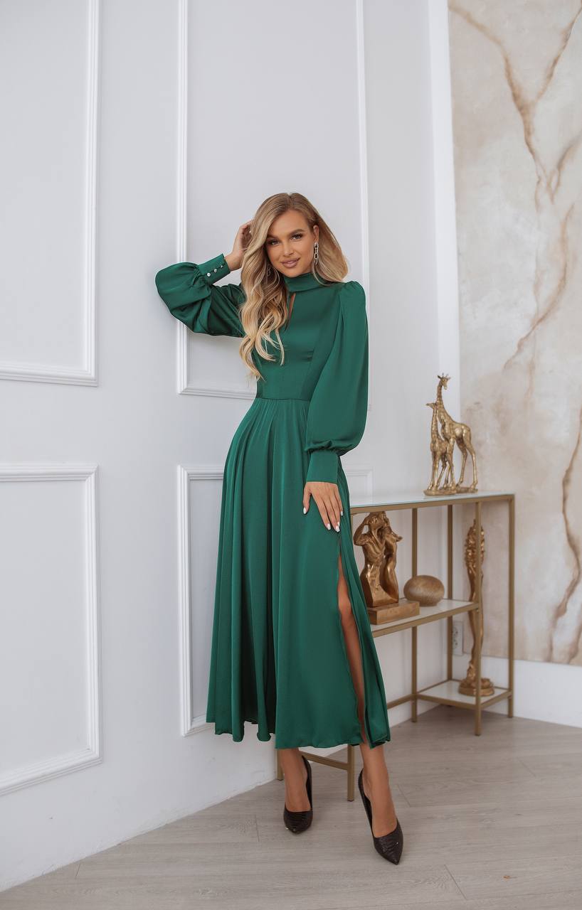 Woman wearing a green dress with a high slit in a room with white paneled walls and a marble accent wall.