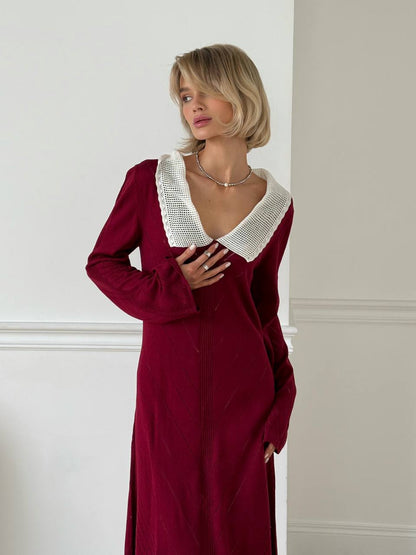 Woman wearing a burgundy dress with a white collar against a neutral wall.