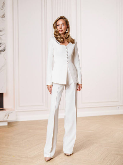 Woman wearing a white suit standing in a room with a white wall and wooden floor.