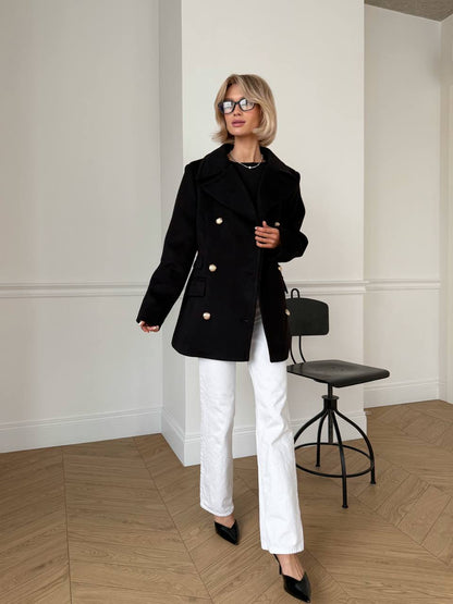 Woman wearing a black coat and white pants in an indoor setting