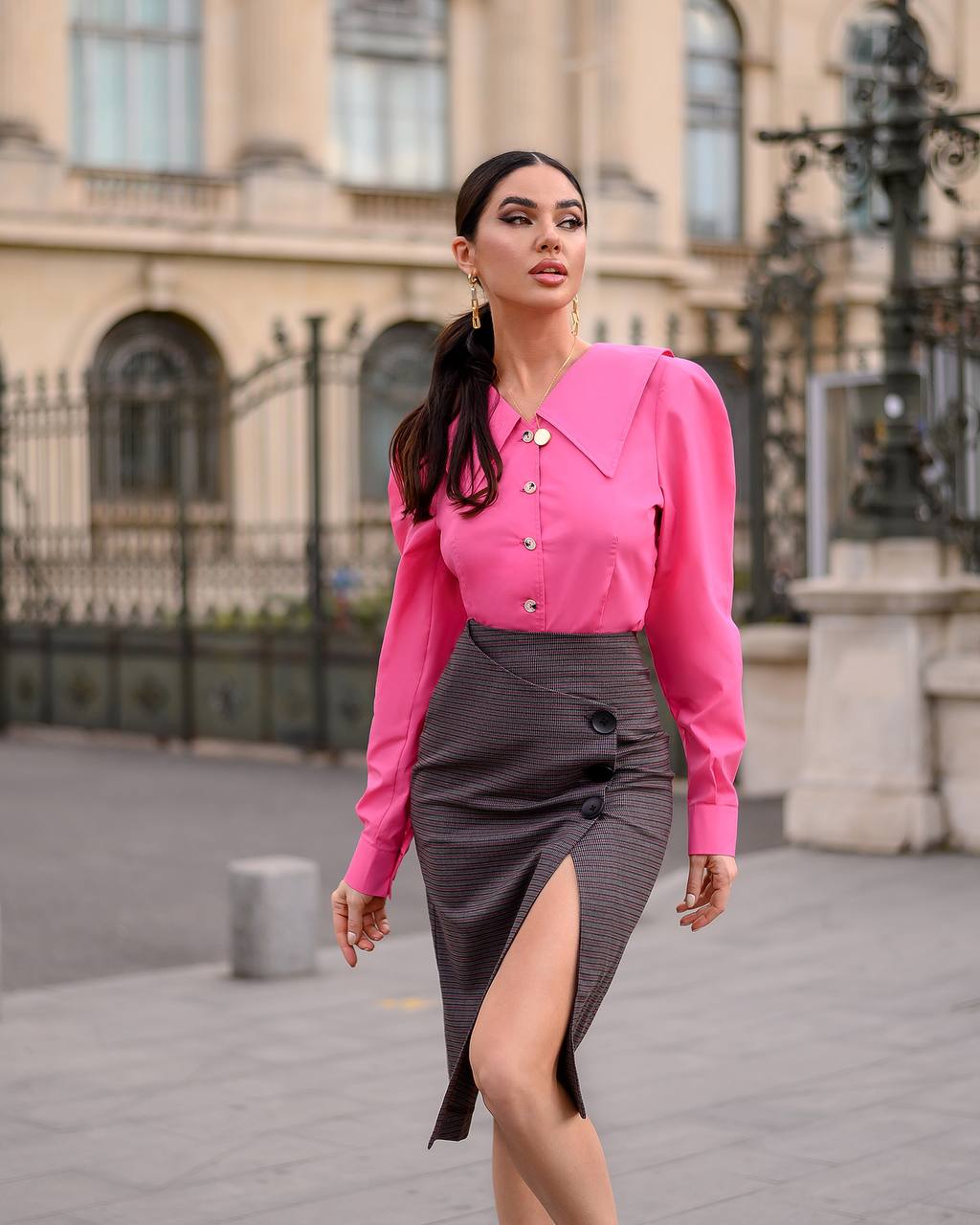 Woman in a pink blouse and gray skirt standing in an urban setting.