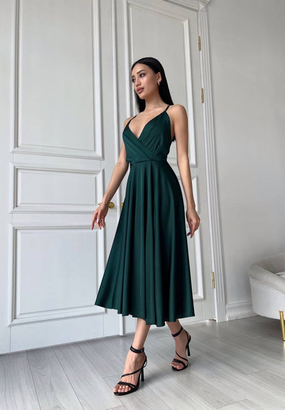 Woman wearing a green dress standing in a room with white walls and a door.