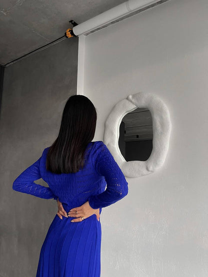 Person in a blue dress standing in front of a white wall with a unique circular object.