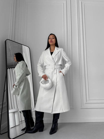 Woman in a white coat standing next to a mirror reflection in a minimalistic setting.