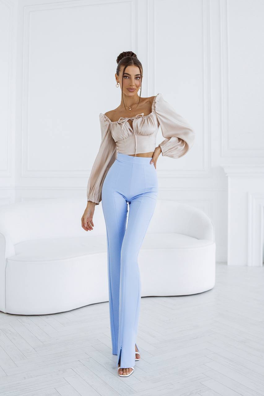 Woman wearing a beige blouse and light blue pants in a minimalistic room.