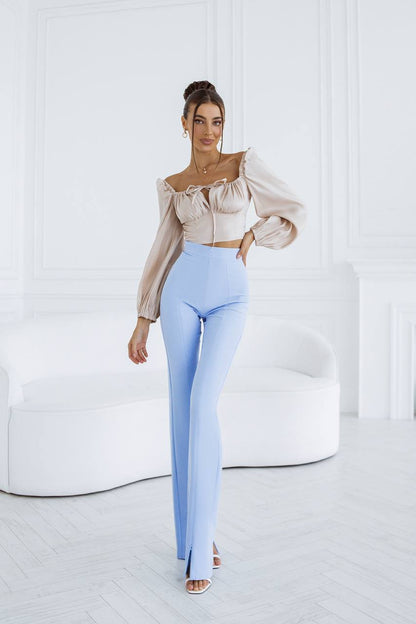Woman wearing a beige blouse and light blue pants in a minimalistic room.