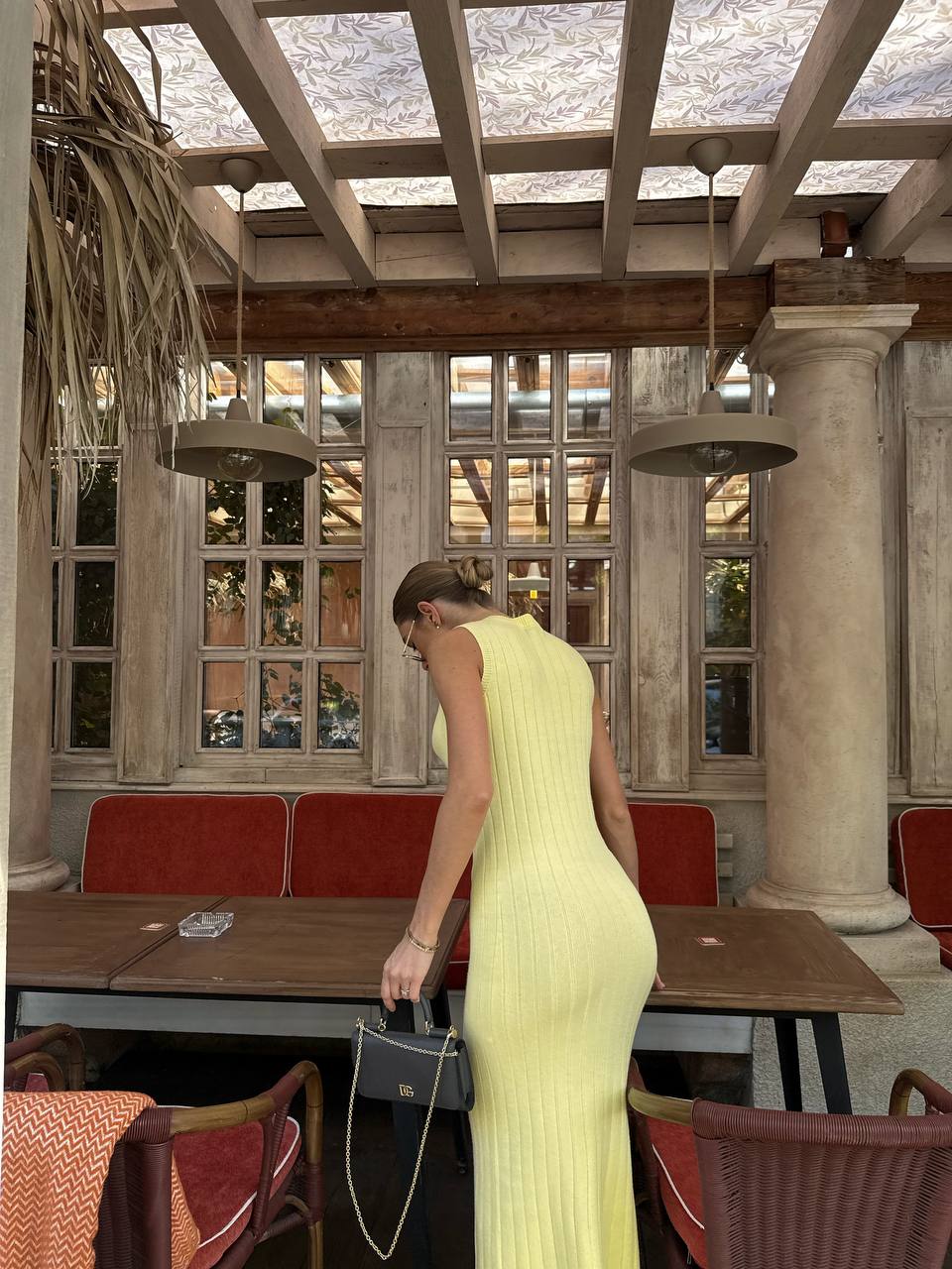 Woman in a yellow dress standing in a room with wooden beams and large windows.