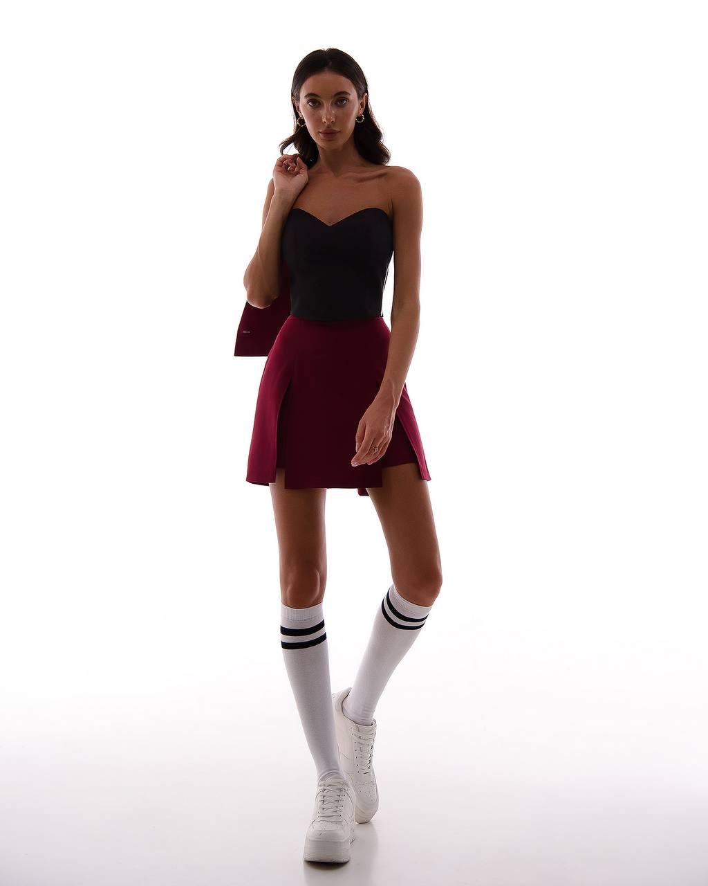 Woman wearing a black strapless top and maroon skirt with white socks and sneakers on a white background