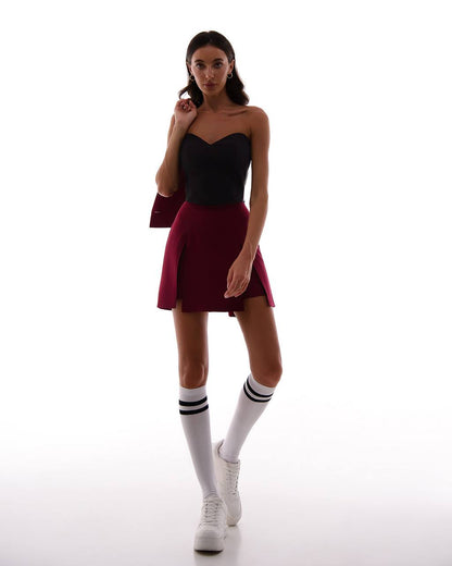 Woman wearing a black strapless top and maroon skirt with white socks and sneakers on a white background
