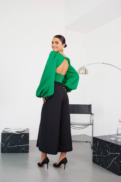 Woman in a green top and black pants standing in a modern interior setting.