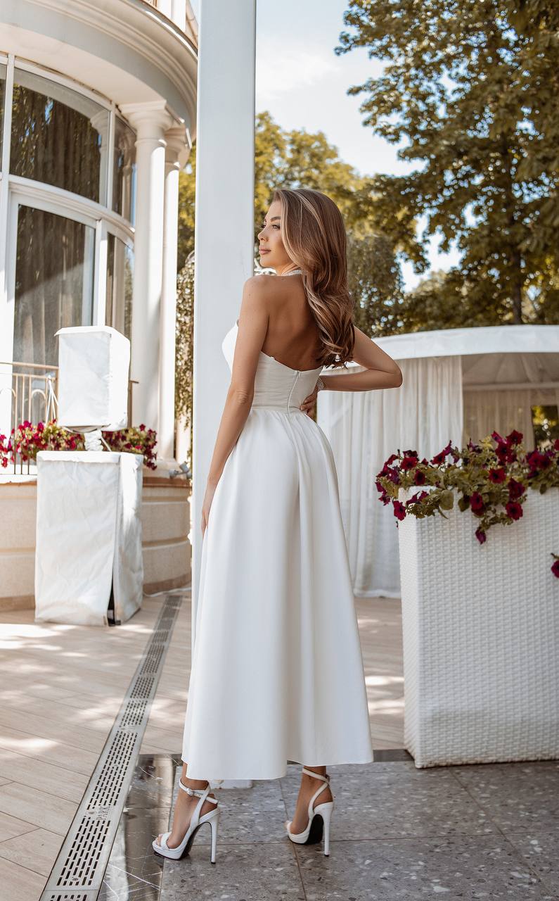 Woman in a white dress standing in an elegant outdoor setting with floral arrangements.