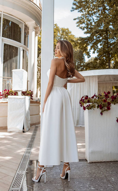 Woman in a white dress standing in an elegant outdoor setting with floral arrangements.