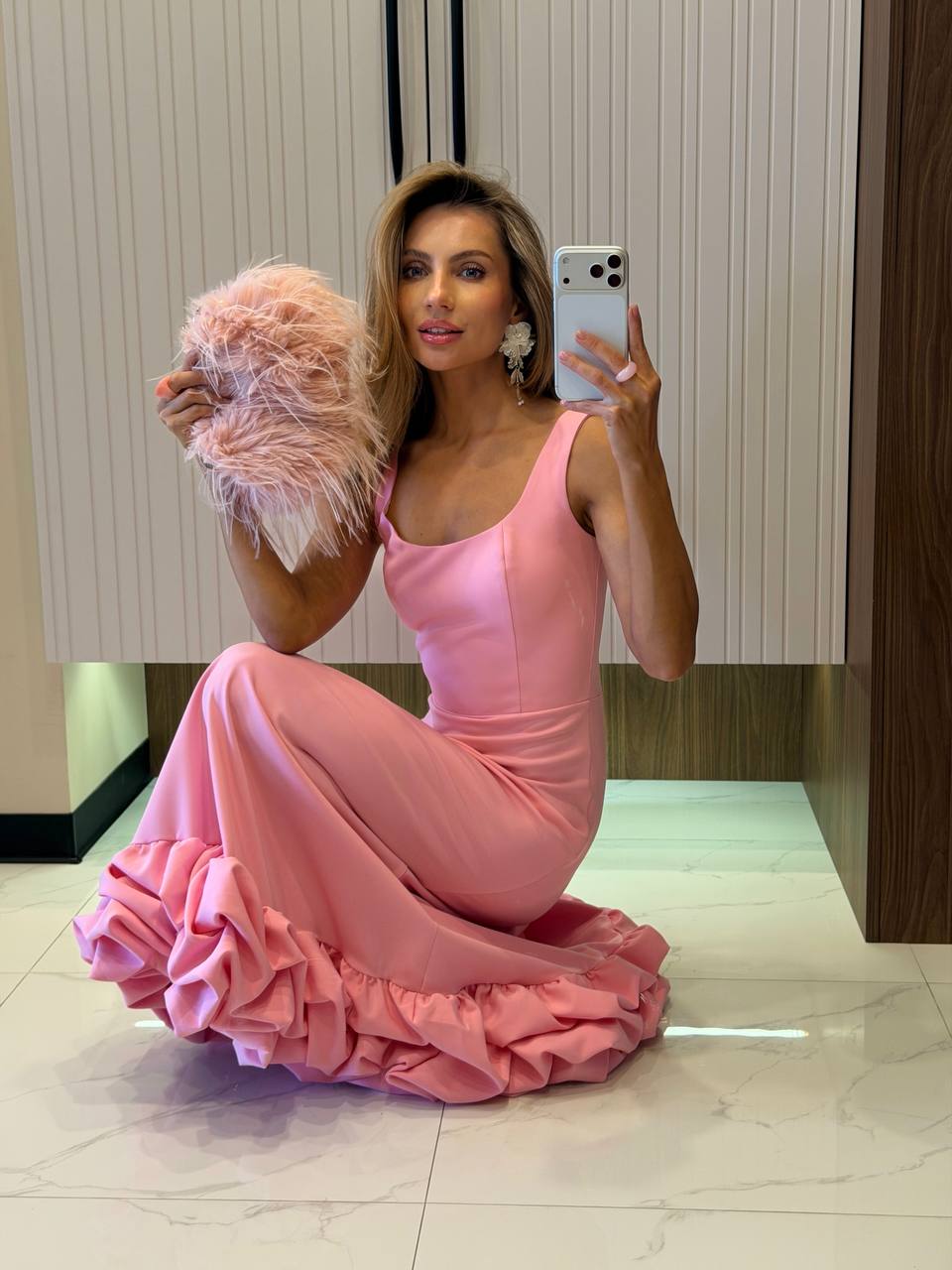 Woman in a pink dress taking a mirror selfie in a room with a wooden floor.