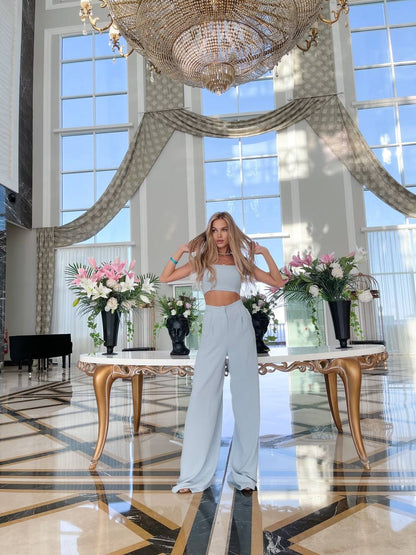 Woman posing in a luxurious room with a chandelier and floral arrangements.