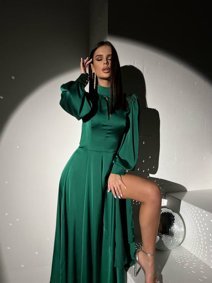 Woman in a green dress posing against a white wall with a spotlight effect.