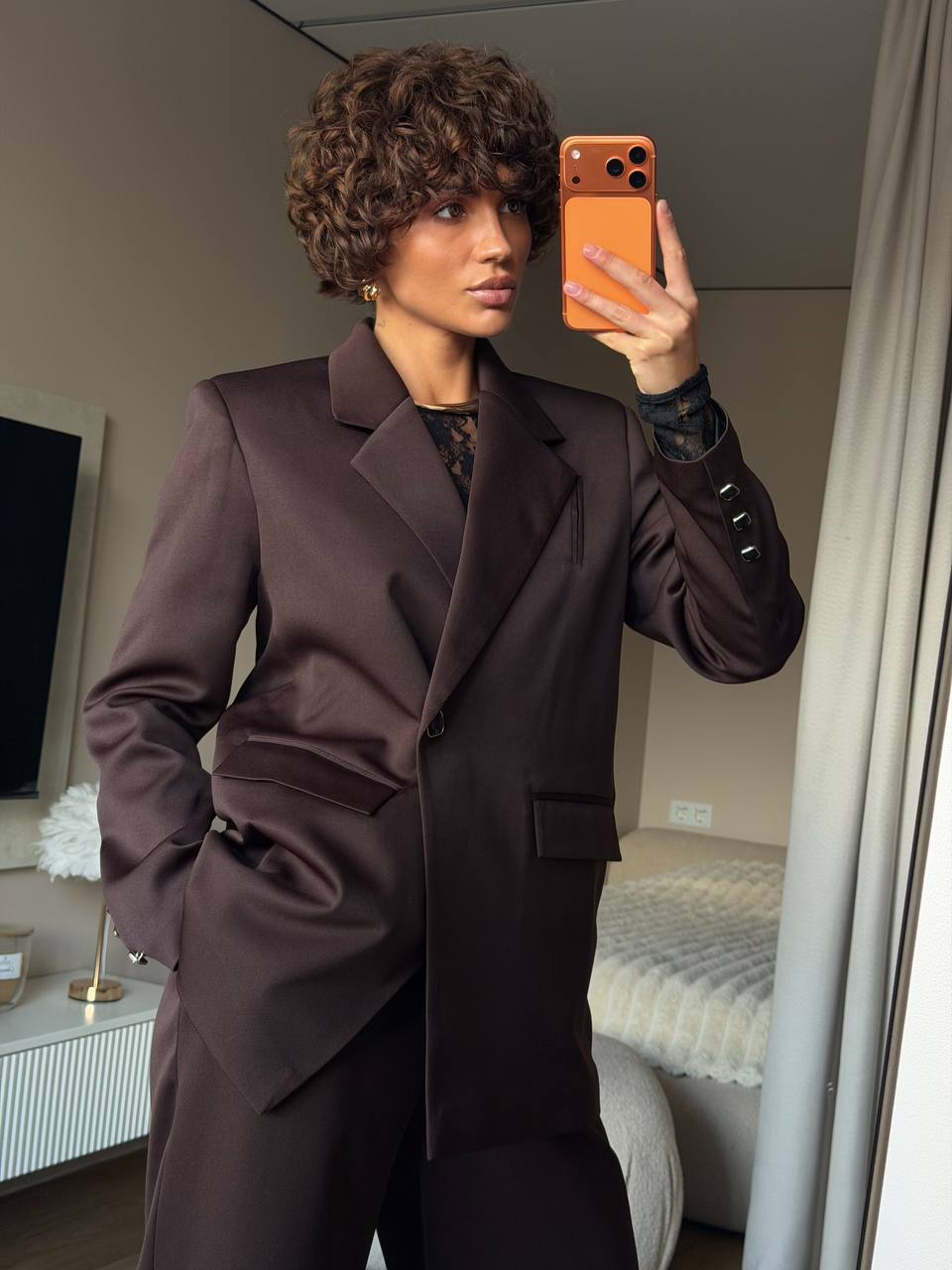 Person taking a mirror selfie wearing a brown coat in a room.