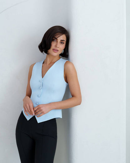 Woman wearing a light blue sleeveless top with buttons against a white background