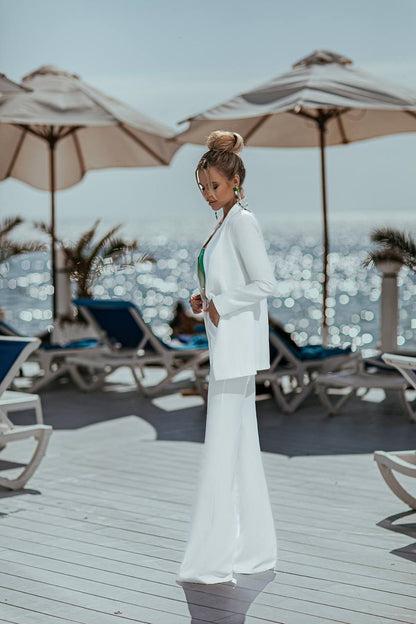 Woman in a white outfit standing on a wooden deck with beach umbrellas and chairs in the background.