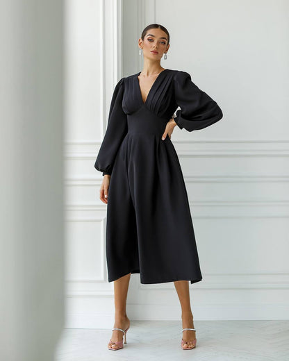 Woman wearing a black dress with long sleeves against a white wall