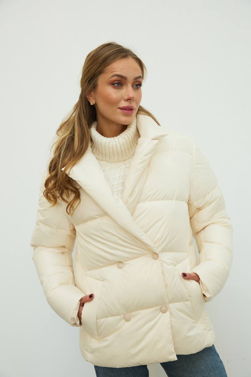Woman wearing a cream puffer jacket and turtleneck against a white background