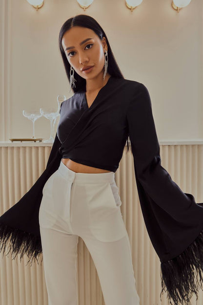 Woman wearing a black fringed jacket over a black top and white pants in an indoor setting.