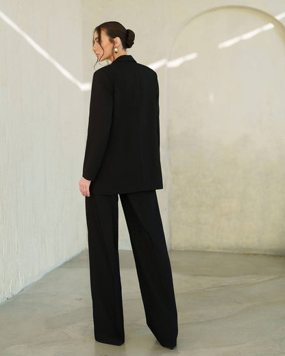 Person wearing a black suit standing in a minimalistic room with white walls and a gray floor.
