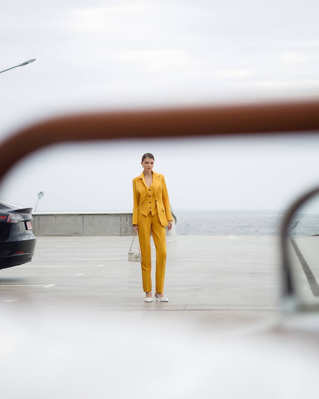 Woman in a yellow suit standing in front of a car with a blurred background
