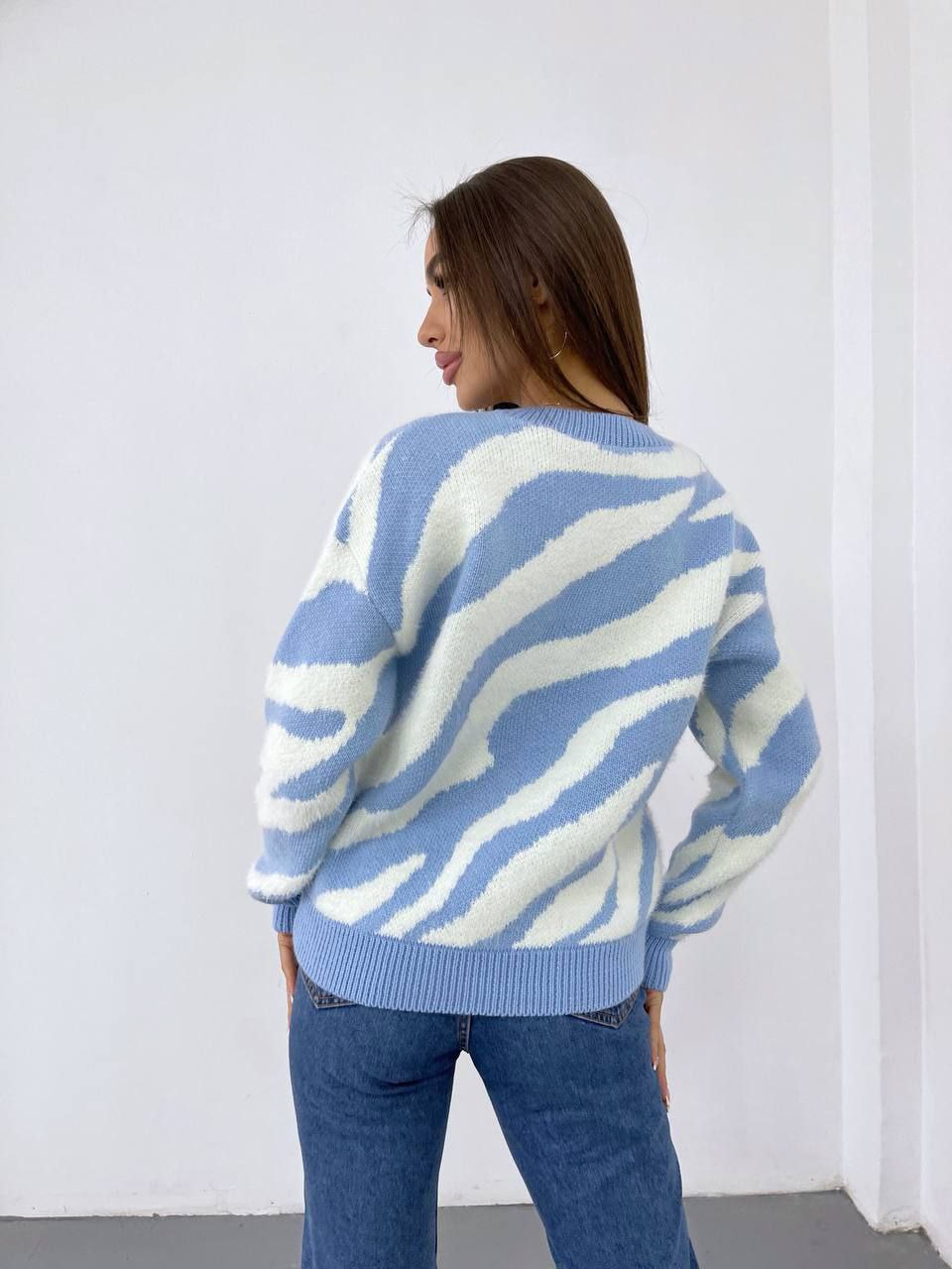 Woman wearing a blue and white patterned sweater against a white wall.