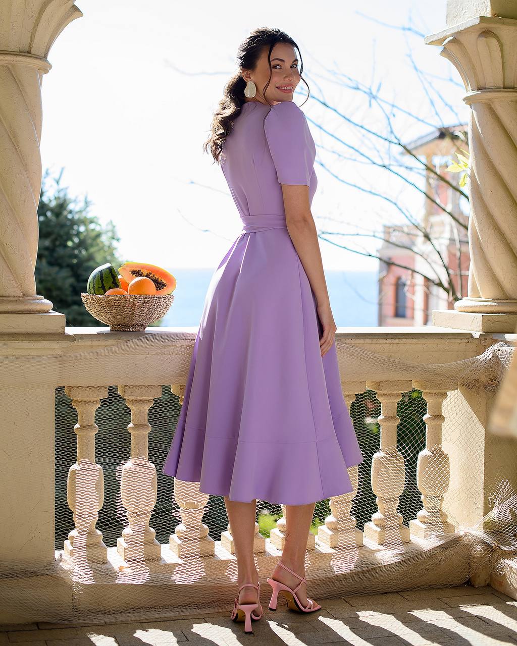 Woman in a purple dress standing on a balcony with a scenic background