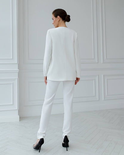 Woman wearing a white suit standing in a minimalistic room with white walls and floor.