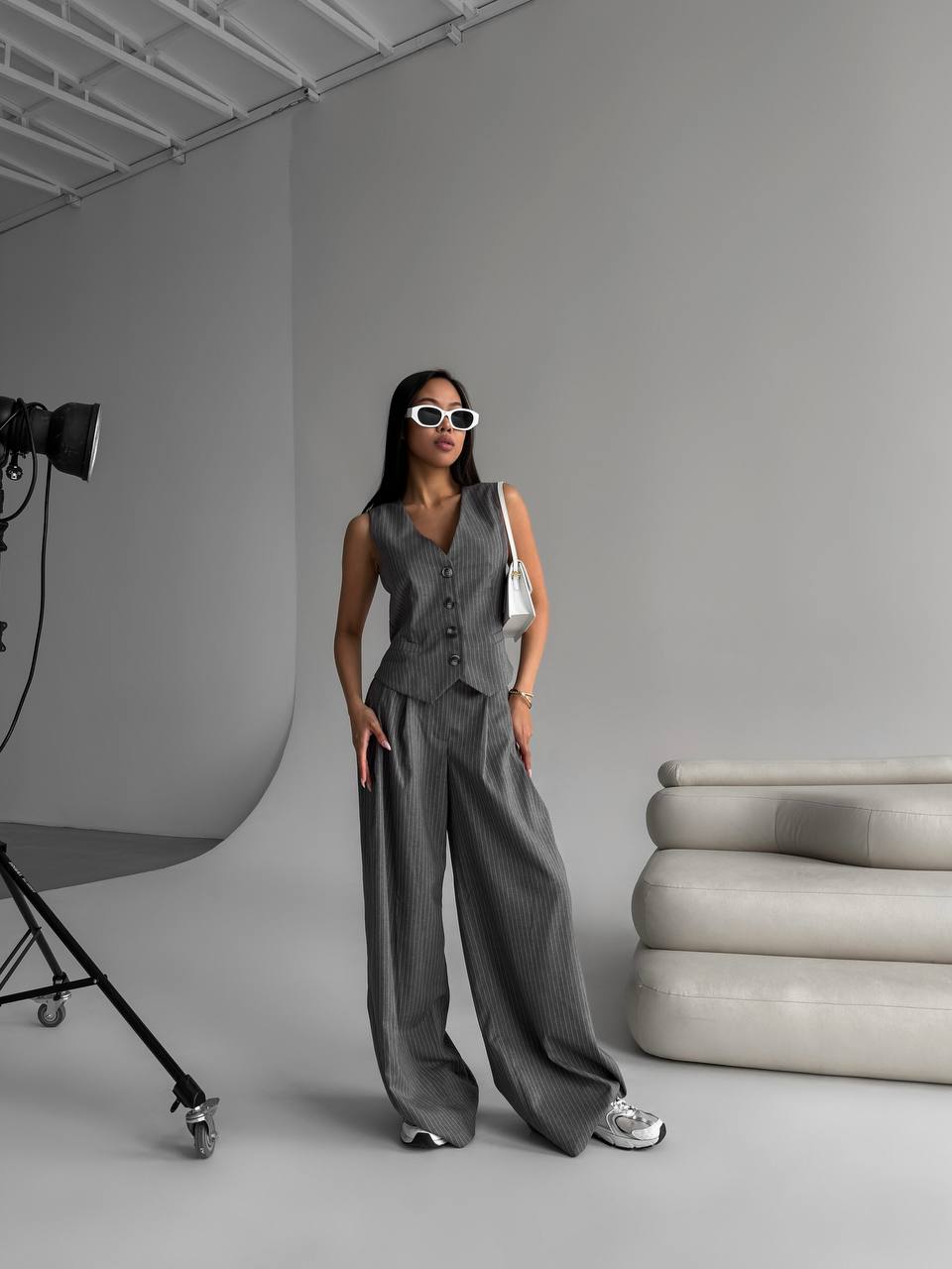 Woman in a gray outfit standing in a studio setting with gray walls and a gray floor.