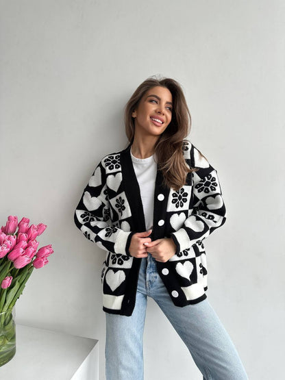 Woman wearing a black and white patterned cardigan with a vase of pink tulips in the foreground.