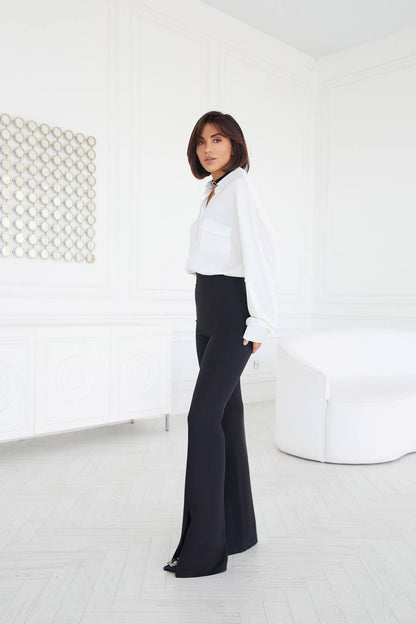 Person wearing a white blouse and black pants in a minimalistic room.