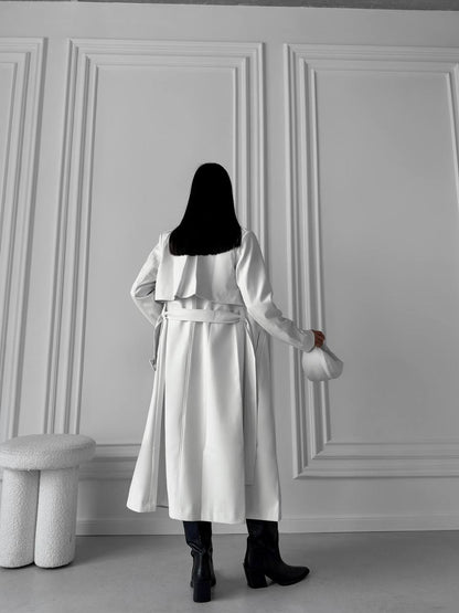Person wearing a white coat standing against a gray paneled wall.