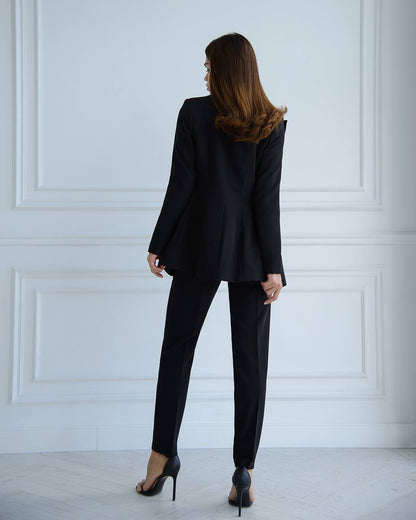 Woman wearing a black suit standing against a white paneled wall.