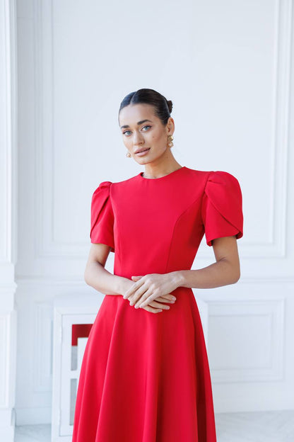 Woman wearing a red dress with puff sleeves against a white wall.