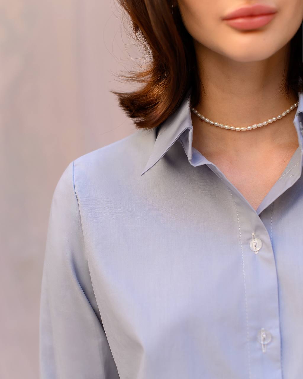 Light blue shirt worn by a person with a pearl necklace against a neutral background