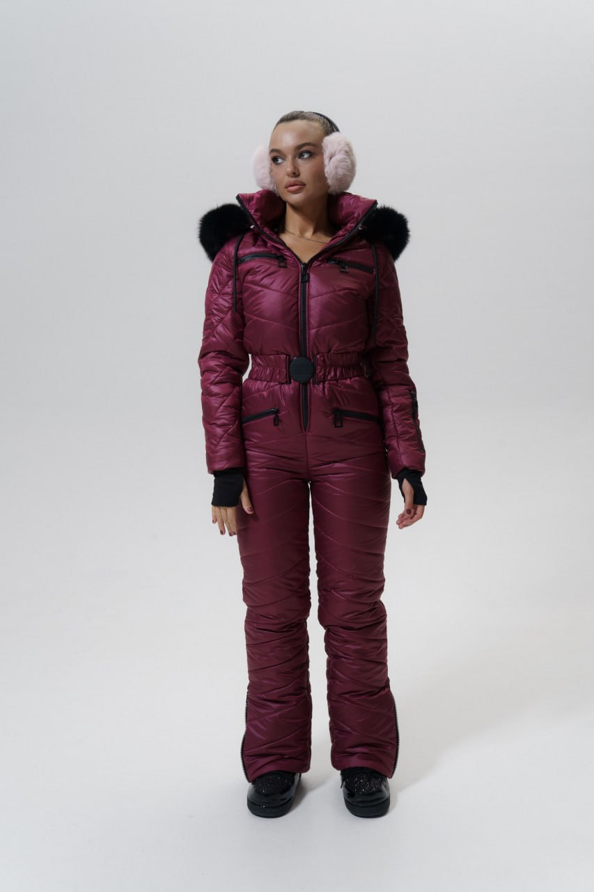 Person wearing a maroon snowsuit with fur-lined hood and pink ear muffs on a white background