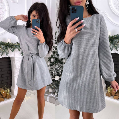 Woman wearing a gray dress in a festive indoor setting with Christmas decorations.