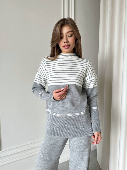 Woman wearing a gray and white striped sweater and pants in a neutral setting