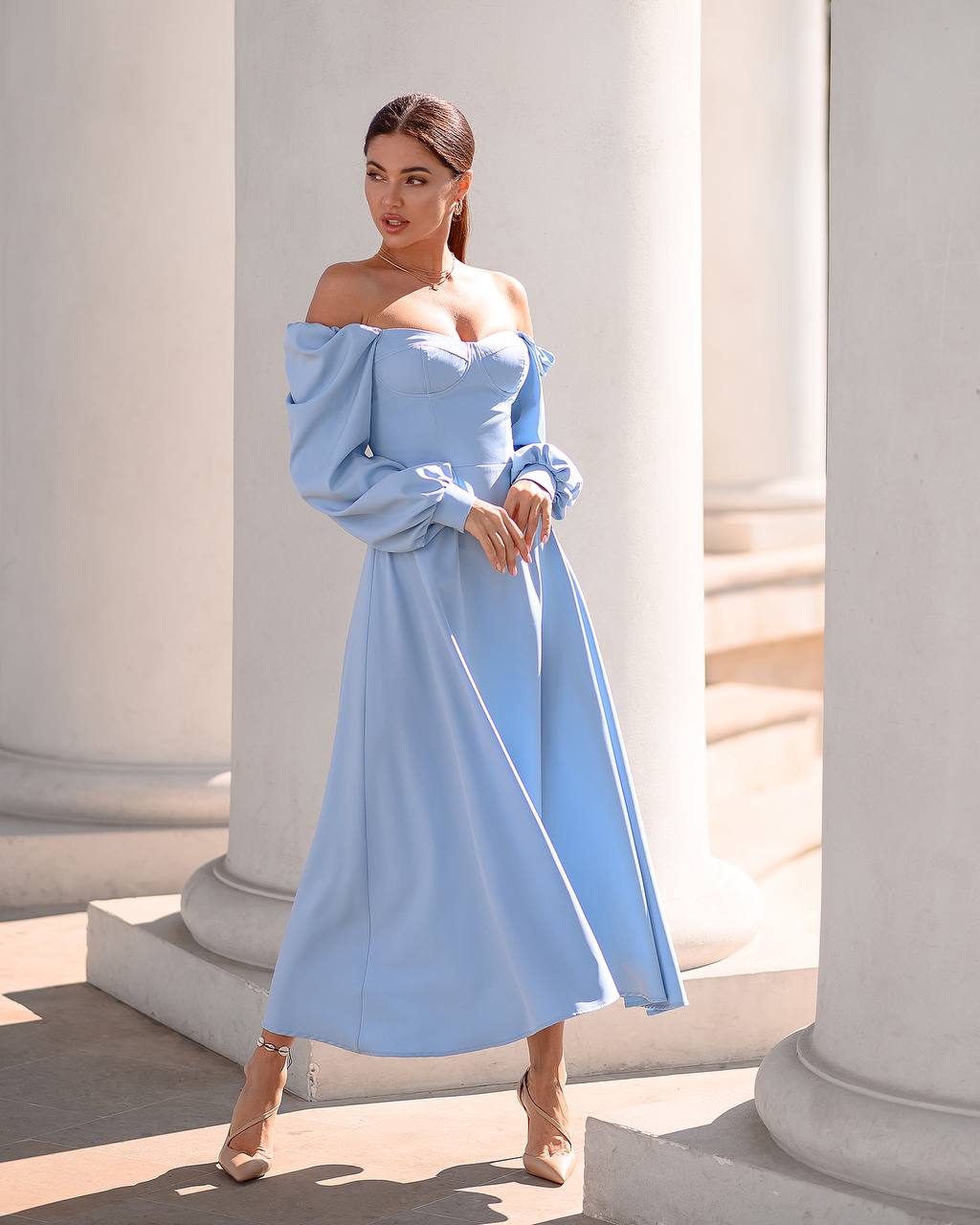 Woman wearing a light blue off-shoulder dress standing in front of classical architecture.