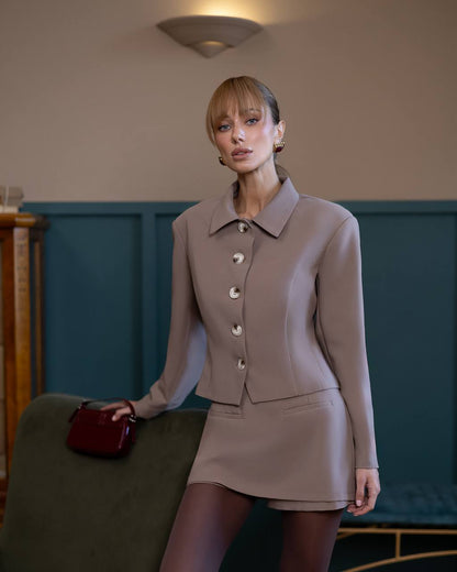 Woman in a beige suit holding a red handbag in an indoor setting