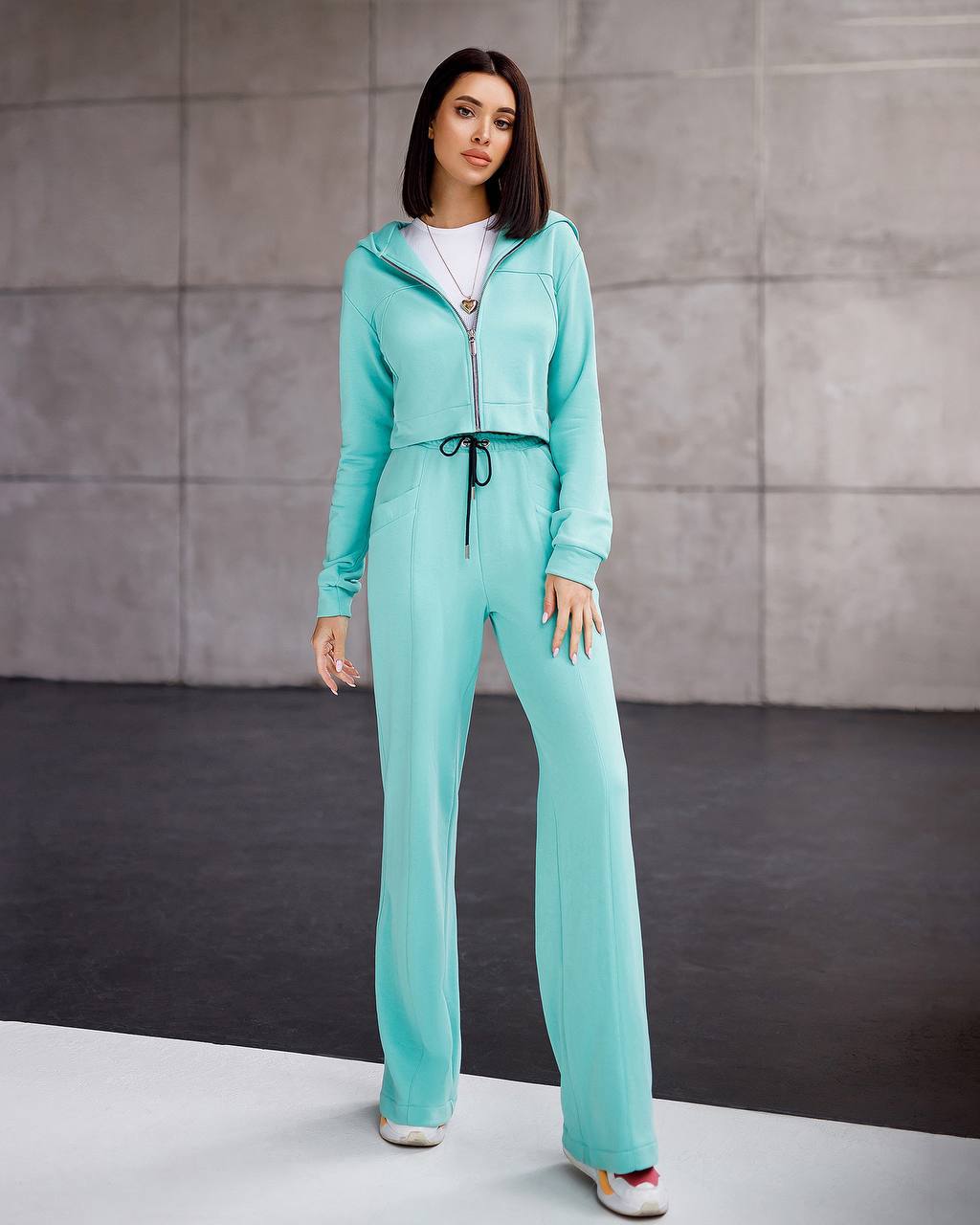 Woman wearing a turquoise tracksuit against a gray background