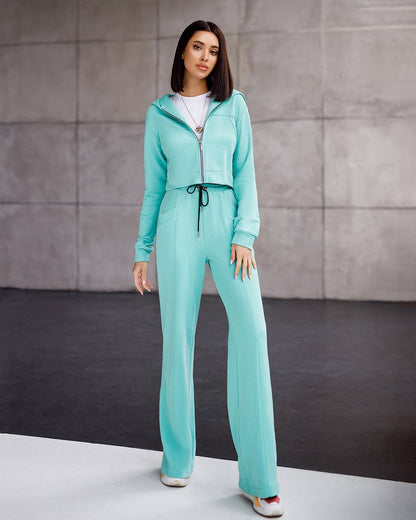 Woman wearing a turquoise tracksuit against a gray background